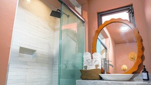 A bathroom with a glass shower enclosure, a white sink with a marble countertop, a wooden-framed mirror, and a bottle of hand soap. - CASA H (San Miguel de Allende)
