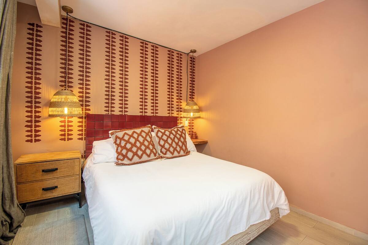 Une chambre d’hôtel comprenant un lit, deux tables de chevet, une petite table et un mur orné d’un motif décoratif.