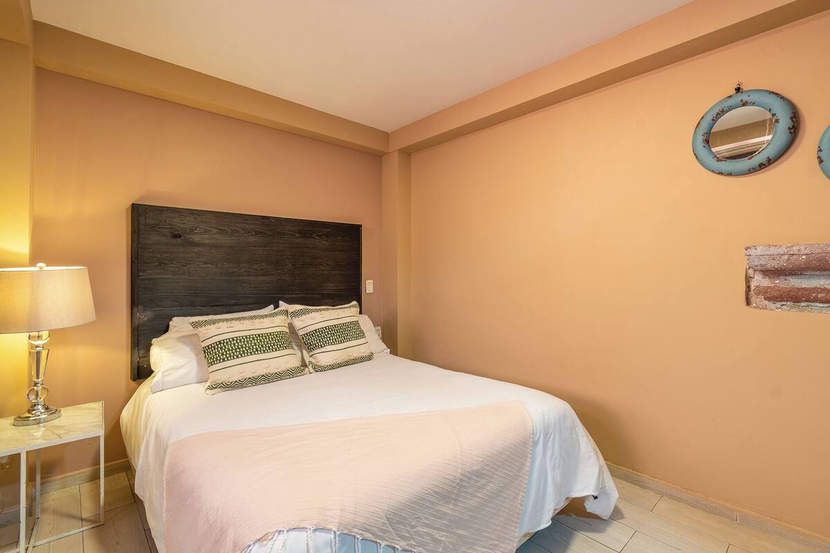 Une chambre à coucher comprenant un lit, une table de chevet, une lampe et deux miroirs fixés au mur.