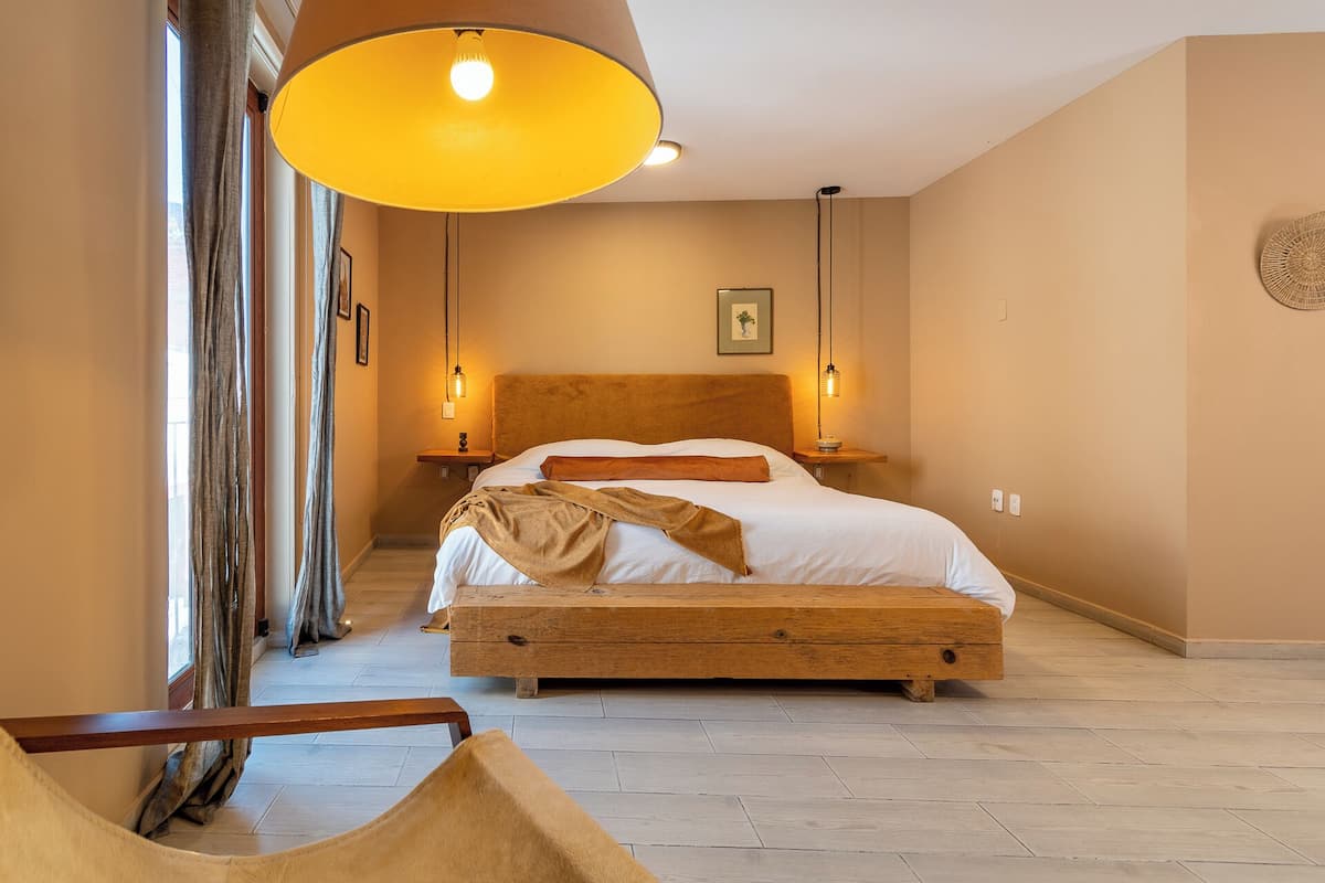 Une chambre avec un lit en bois, deux tables de chevet, une lampe suspendue et une vue sur le couloir.