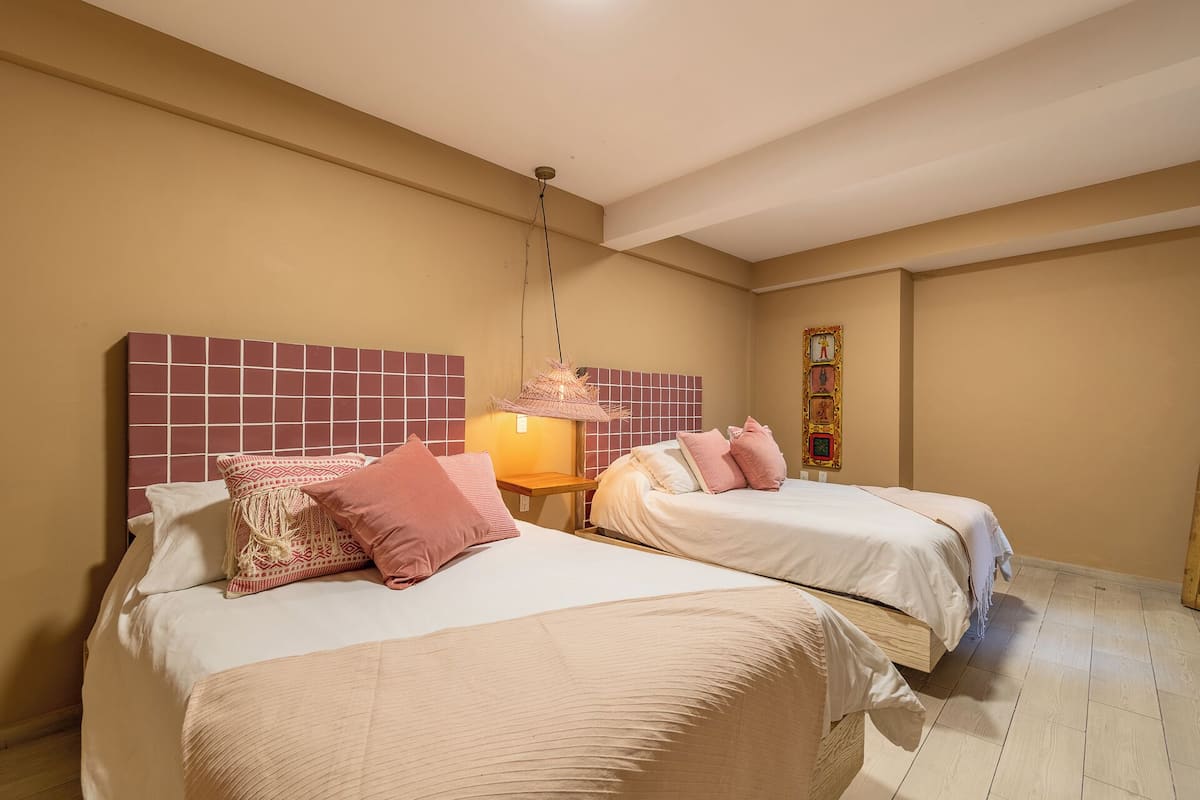 Une chambre d’hôtel avec deux lits, une petite table de chevet, une lampe suspendue et un élément décoratif fixé au mur.