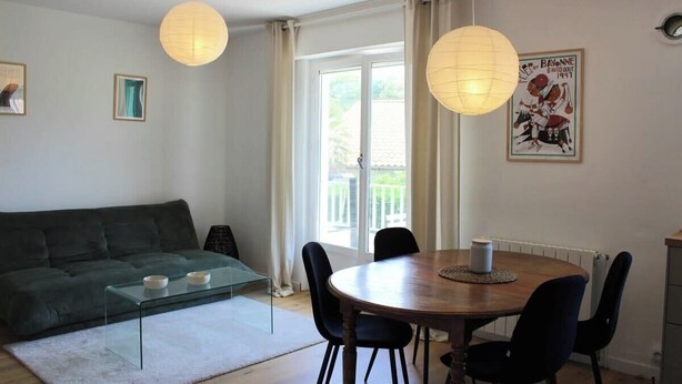 Un salon comprenant un canapé, une table basse en verre, une table à manger en bois avec des chaises, et une grande fenêtre avec des rideaux.