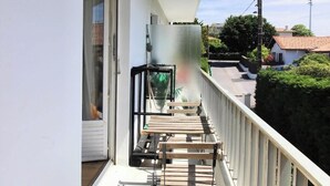 Un balcon avec une table et des chaises, une plante suspendue et une vue sur le quartier.