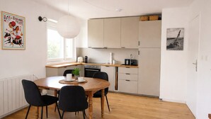 Une cuisine moderne avec un coin repas, comprenant une table ronde en bois, des chaises noires et un luminaire suspendu.