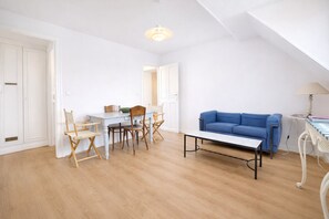 En rummelig stue med spiseplads, en blå sofa og en lampe.