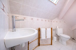 Et badeværelse med hvid vask, bambus-håndklædeholder, toilet og flisebeklædte vægge.