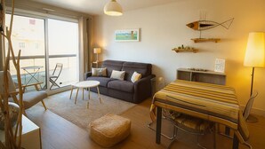 Un salon moderne avec un canapé, une table à manger, une lampe et une vue dégagée sur l’extérieur grâce à une grande fenêtre.