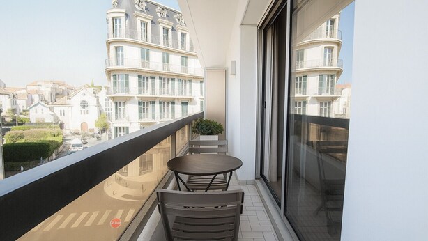 Un balcon avec une table et des chaises, une plante en pot et une vue sur les immeubles.