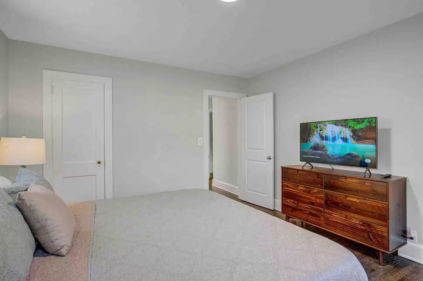 A bedroom with a bed, a dresser, a television, and two doors.