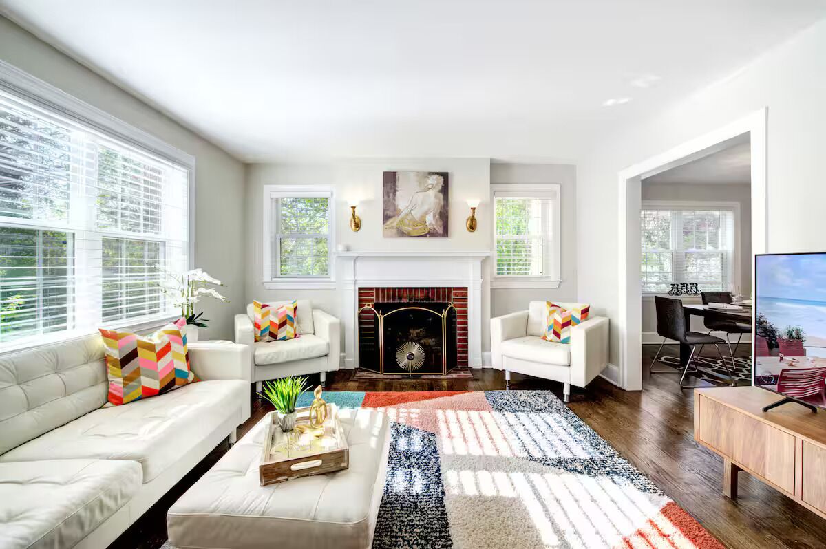 A modern living room with a fireplace, white sofas, and a large window.