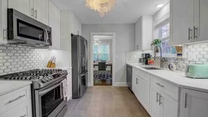 Una cocina moderna con electrodomésticos de acero inoxidable, armarios blancos y una lámpara de araña.