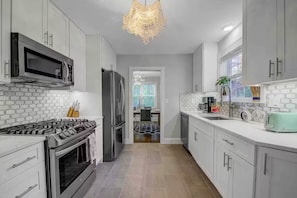 A modern kitchen with stainless steel appliances, white cabinetry, and a chandelier.