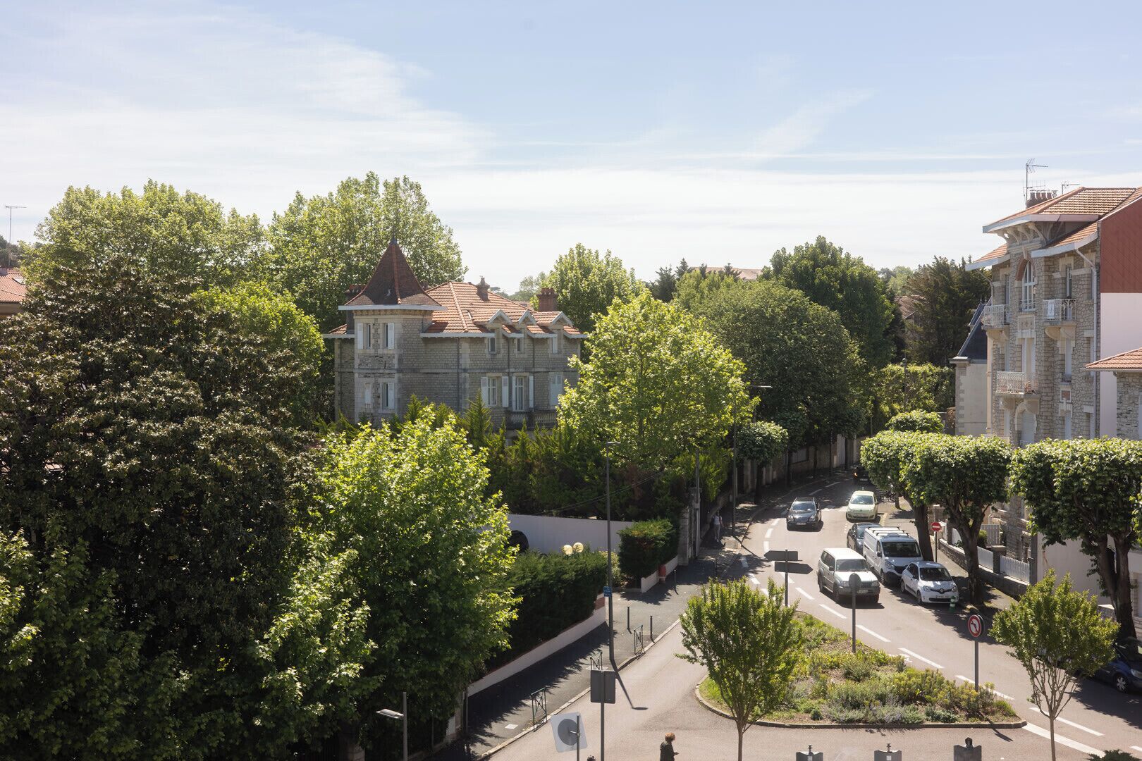 Vista de una calle con edificios, árboles y coches aparcados.