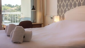 A hotel room with a bed, two towels, a desk with a lamp, and a view of the outdoors. - Cosy apartment with Balcony near the Beach (Biarritz)