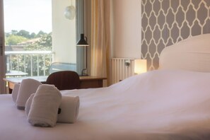 A hotel room with a bed, two towels, a desk with a lamp, and a view of the outdoors. - Cosy apartment with Balcony near the Beach (Biarritz)