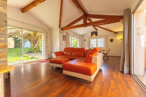 A spacious living room with a large orange leather sofa, wooden beams, and large windows offering a view of the outdoors. - Charming House with Garden in Biarritz (Biarritz)