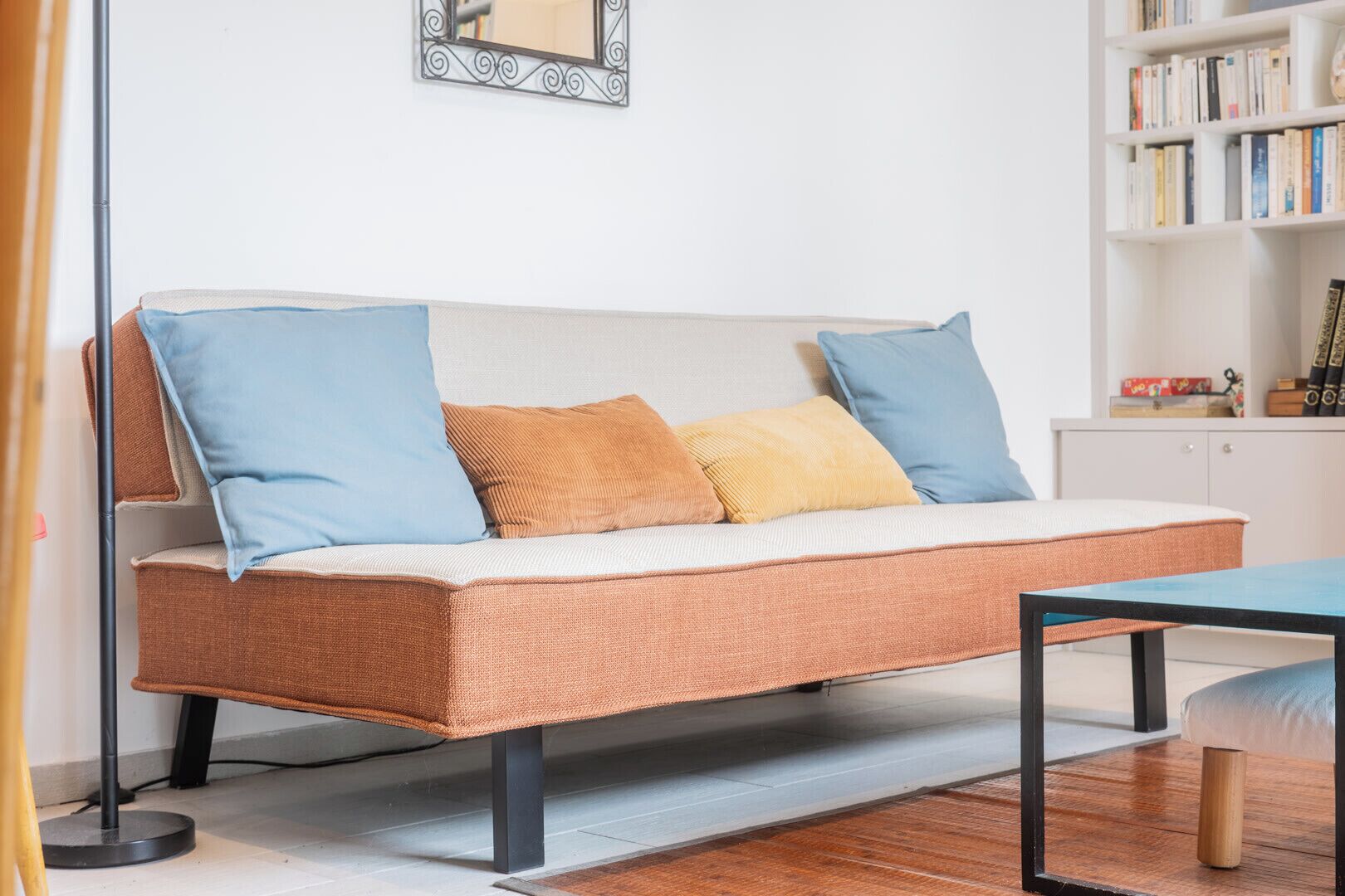 A sofa with cushions, a table, and a bookshelf with books.