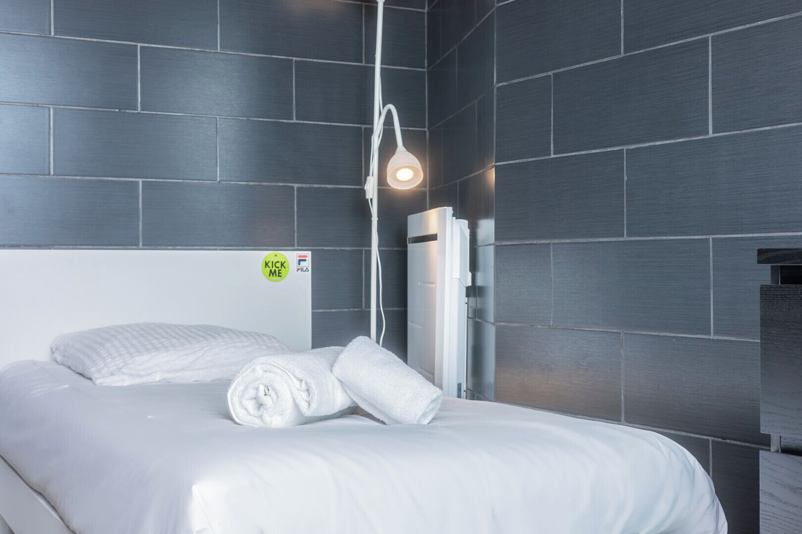 Moderni hotellihuone, jossa on suuri sänky, seinään kiinnitetty valaisin ja näkyvissä oleva ilmastointilaite.