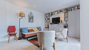 Una sala de estar moderna con un sofá, dos sillones, una butaca roja, una lámpara de pie, un televisor y una estantería.