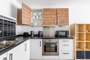 A modern kitchen with white cabinets, a stainless steel sink, a coffee maker, a kettle, a microwave, and an oven. - Blueground | Poplar, balcony, nr Thames (London)