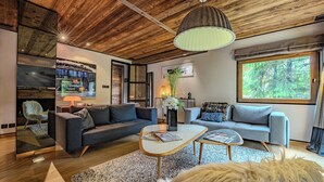 A modern living room with a wooden ceiling, a fireplace, a sofa, a coffee table, and a large window. - Rochebrune (Megève)
