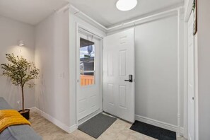 A hallway with a white door, a potted plant, and a grey carpet. - Charming 4-bedroom house with AC in vibrant Calgary (Calgary)