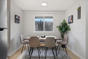 Un coin repas comprenant une table, quatre chaises, une plante en pot et une fenêtre donnant sur un paysage agréable.