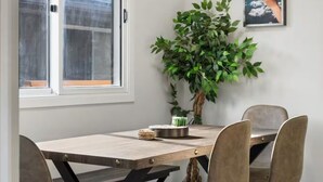 En matplats med ett träbord, fyra stolar, en krukväxt och en inramad tavla på väggen.
