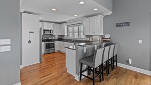 A kitchen with white cabinets, a central island with bar stools, a stainless steel oven, and a window with blinds. - "2ice As Nice" - 4 Bedrooms, 3.5 Bathrooms, Private Pool (Holden Beach)