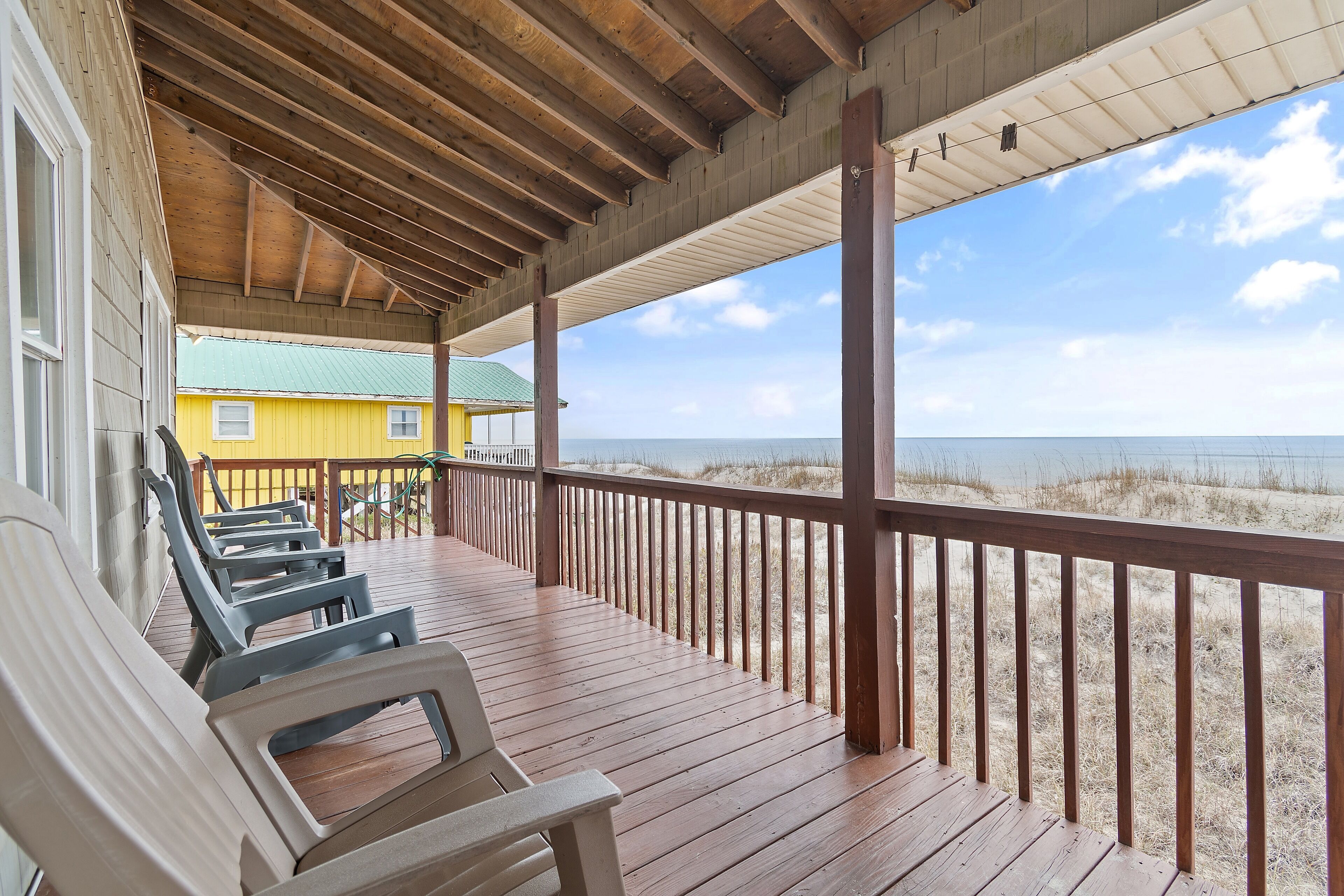 A wooden deck with chairs, a railing, and a view of the beach and ocean.