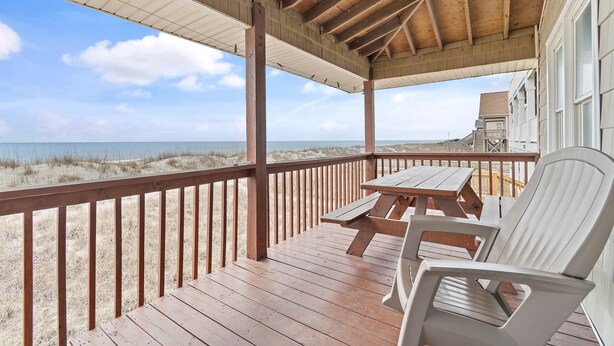A wooden deck with a table and chairs, overlooking a beach with dunes and the ocean. - "Charisma"  4 Bedroom, 2 Bathroom, Oceanfront (Holden Beach)