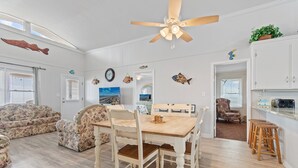 A spacious living room with a wooden dining table, floral sofas, a ceiling fan, and nautical-themed wall decorations. - "Charisma"  4 Bedroom, 2 Bathroom, Oceanfront (Holden Beach)