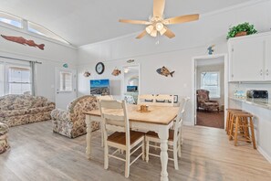 A spacious living room with a wooden dining table, floral sofas, a ceiling fan, and nautical-themed wall decorations. - "Charisma"  4 Bedroom, 2 Bathroom, Oceanfront (Holden Beach)