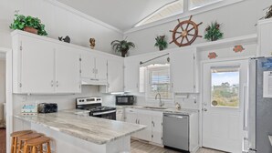A kitchen with white cabinets, a central island with stools, a microwave, stove, and dishwasher. - "Charisma"  4 Bedroom, 2 Bathroom, Oceanfront (Holden Beach)