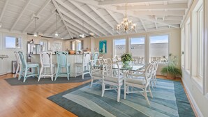 A spacious kitchen with white cabinetry, a dining area with white chairs, and a large window providing natural light. - "Goins My Way" 6 Bedrooms, 6.5 Bathrooms, Private Pool and Elevator (Holden Beach)