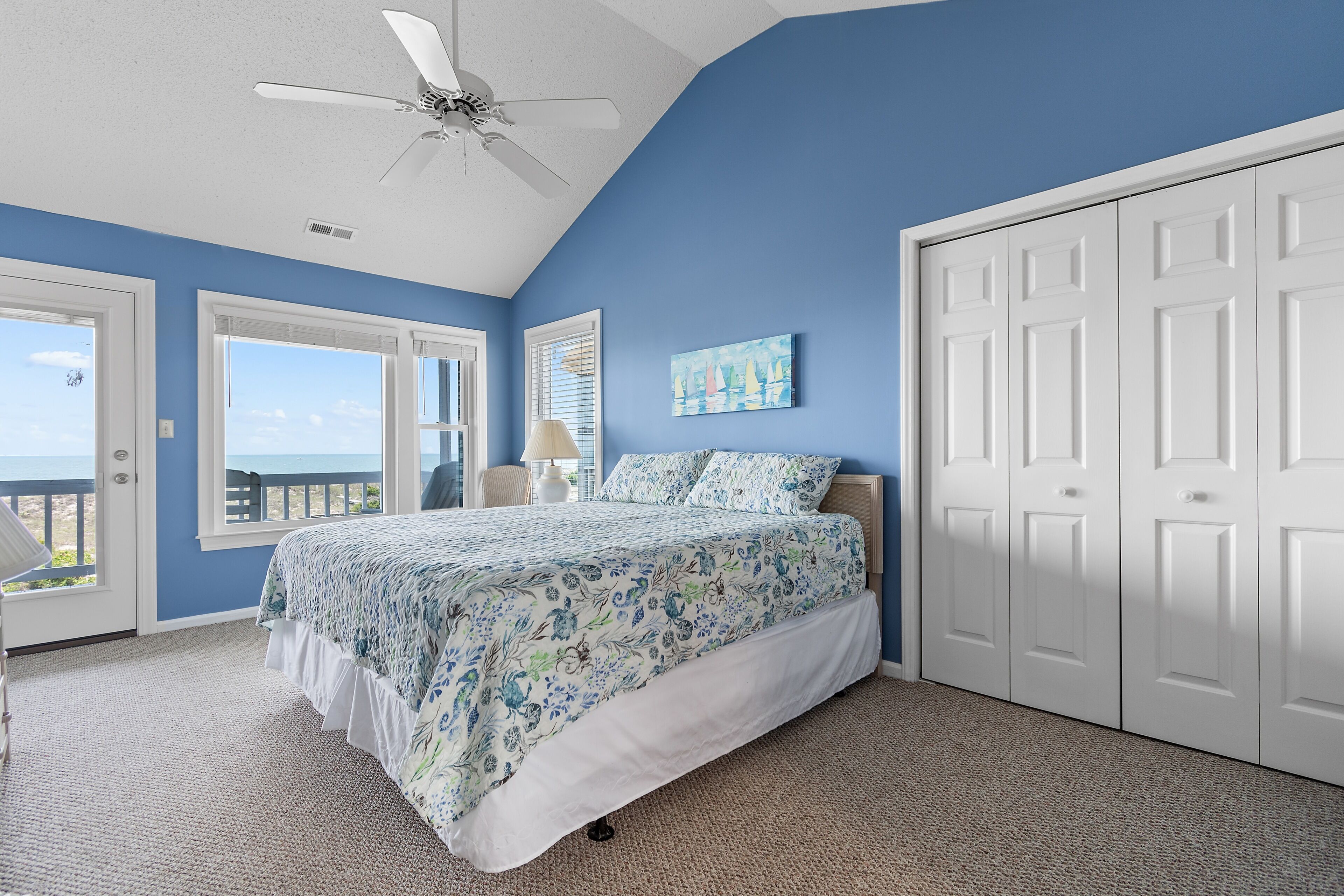 A bedroom with a bed, a ceiling fan, a painting, and a view through a door.