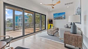 A modern living room with a large sliding glass door to a deck, a ceiling fan, a sofa, a coffee table, and a lamp. - 5 Bedrooms, 5 Bathrooms, Private Pool (Holden Beach)
