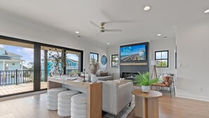 A spacious living area with a large TV, a ceiling fan, and a balcony with a view of other houses. - 5 Bedrooms, 5 Bathrooms, Private Pool (Holden Beach)