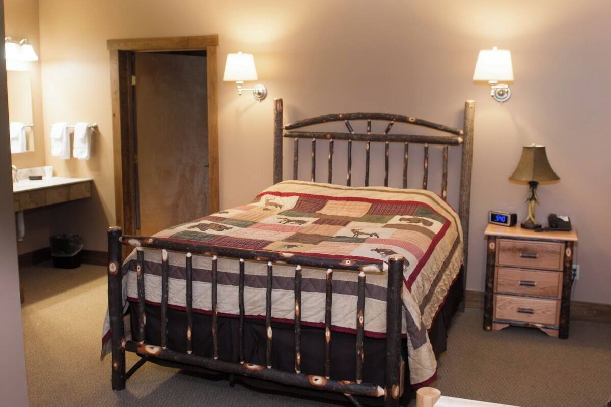 Un lit en bois avec une courtepointe, une table de chevet avec une lampe et une horloge fixée au mur.