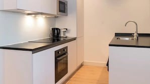 A compact kitchen with white cabinets, a microwave, a stove, and a sink. - Cozy apartment canal view (Amsterdam)