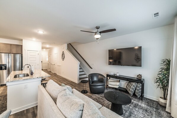 A modern kitchen with a built-in refrigerator, a dining area with a black chair and table, and a living room with a sofa and a TV. - Chic Huntsville Stay: Near MidCity, Dining & Shops (Huntsville)