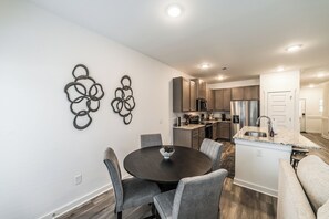 A modern kitchen with dark cabinets, a central island with a sink, and a dining area with a round table and chairs.