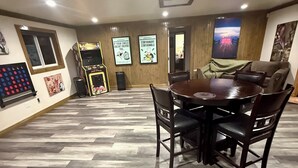 A dining area with a wooden floor, a round table with chairs, and wall decorations including posters and a framed picture. - Large 6BR with Game Room, Perfect for Large Families & Groups, Forks PNW Retreat (Forks)