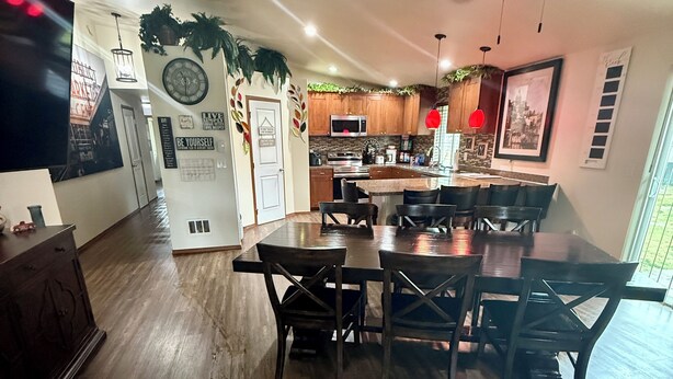 A spacious living room with a large wooden dining table and chairs, a kitchen with wooden cabinets and a microwave, and a ceiling fan. - Large 6BR with Game Room, Perfect for Large Families & Groups, Forks PNW Retreat (Forks)