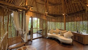 A room with a curved sofa, a wooden bench, and a small table. - Asep Gumi Bamboo Villa Pesagi (Bali)