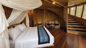 A room with a bed, a small table, and a chair, a staircase, and a large window. - Asep Gumi Bamboo Villa Pesagi (Bali)
