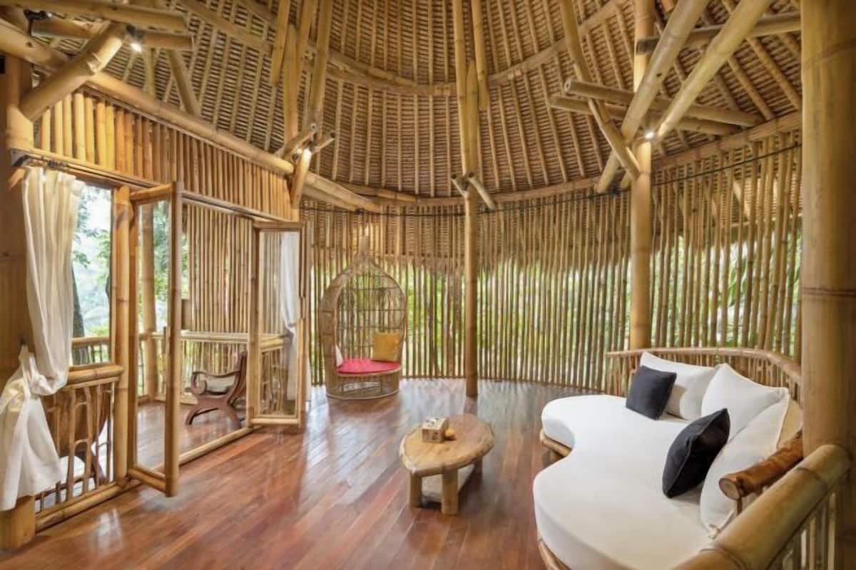 A bamboo-themed room with a bed, a small table, a hanging chair, and a view through the bamboo walls.