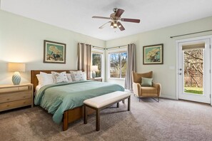 A bedroom with a bed, a chair, a bench, a ceiling fan, and two windows with curtains.