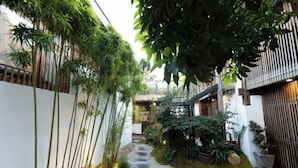 A narrow pathway flanked by bamboo and potted plants, leading to a building with a thatched roof. - ‌The Secret Garden of Cats & Wolf's Den Barista Courtyard Cafe & Inn (Wuyi Street) (Lijiang)