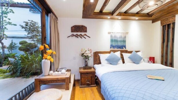 A bedroom with a bed, bedside tables, a nightstand, a window with a view, and a wooden ceiling. - ‌The Secret Garden of Cats & Wolf's Den Barista Courtyard Cafe & Inn (Wuyi Street) (Lijiang)